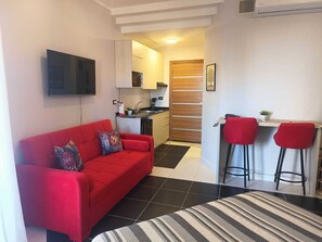 A compact living space with a red sofa, a striped rug, a kitchen area, and two red bar stools. - Royal Beach Resort (Hurghada)