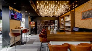 Zona de bar con mostrador de madera, sillas de cuero, candelabro y pantalla de televisión.