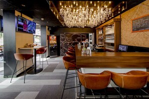 Zona de bar con mostrador de madera, sillas de cuero, candelabro y pantalla de televisión.