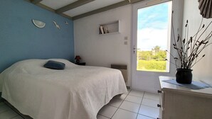 Ein Schlafzimmer mit Bett, Nachttisch, Fenster mit Aussicht und einer Zimmerpflanze.