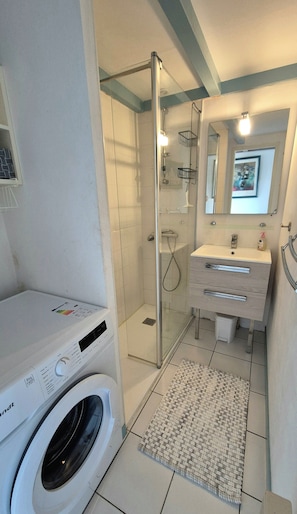A compact bathroom with a glass-enclosed shower, a washing machine, a sink, and a mirror.