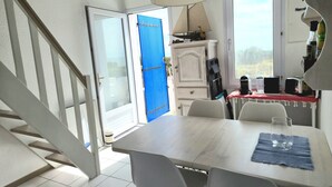 Ein Zimmer mit Esstisch, Stühlen, einer Treppe, einer blauen Tür und einem Fenster.