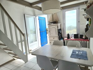 A room with a dining table, chairs, a staircase, a blue door, and a window.
