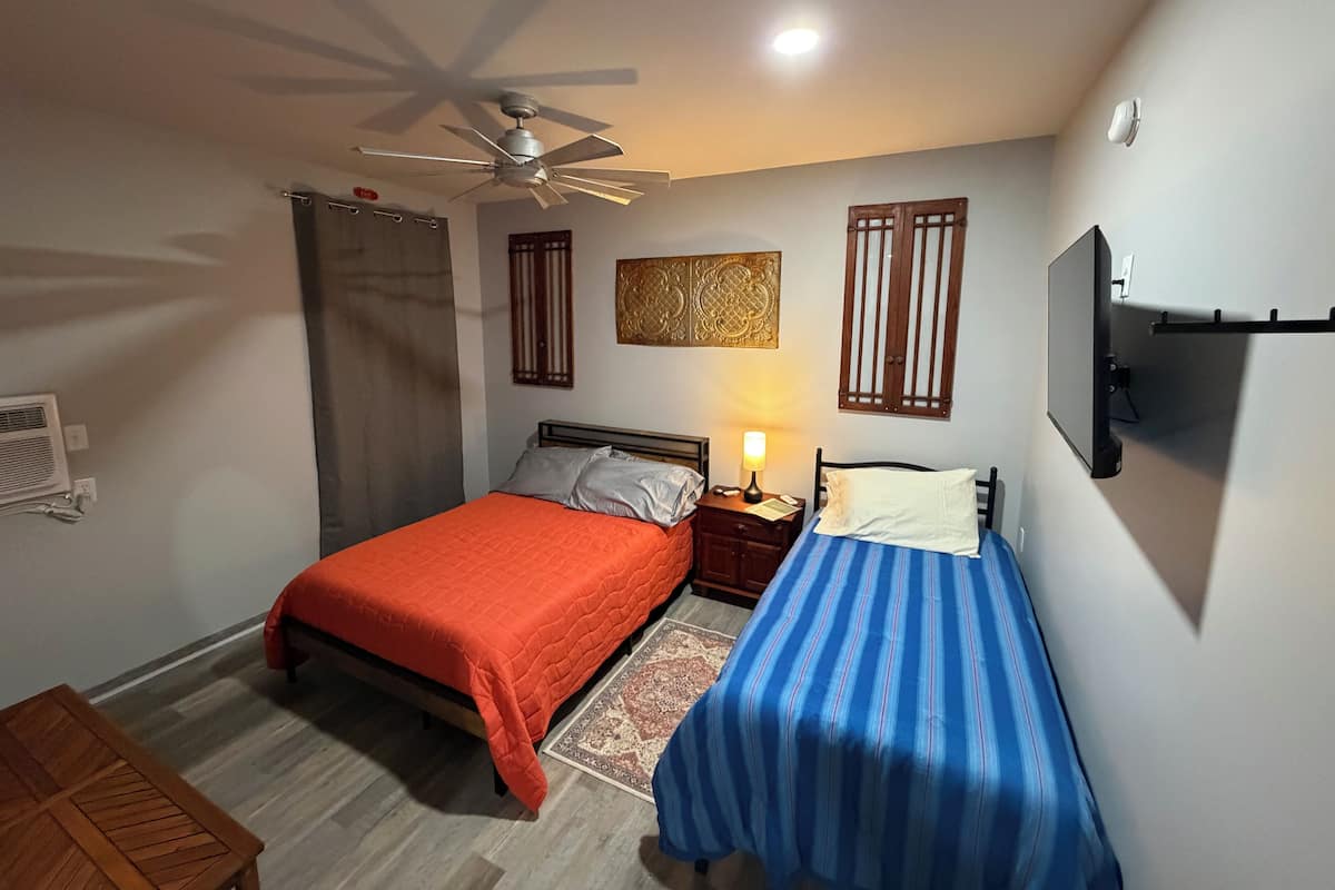 A bedroom with two beds, a ceiling fan, a TV, and a nightstand with a lamp.