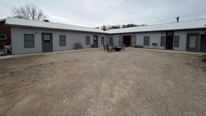 En byggnad med en grusbelagd innergård, flera dörrar och en sittplats med stolar och ett bord.