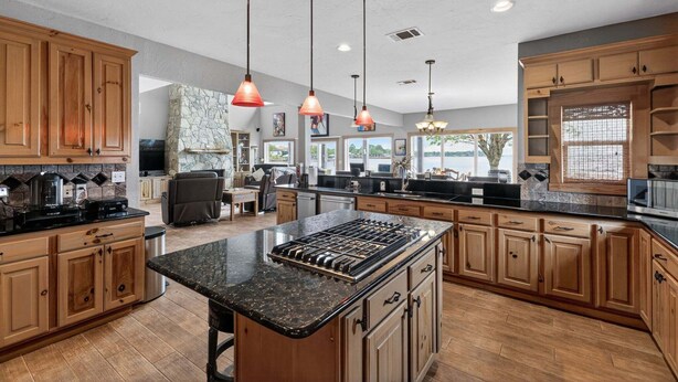 A spacious kitchen with wooden cabinets, a central island, pendant lighting, and a stone fireplace. - Dream Lake House 5br Sleeps 12 Tool Tx 5 Bedroom Home (Kemp)