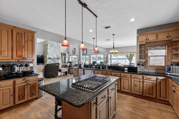 A spacious kitchen with wooden cabinets, a central island, pendant lighting, and a stone fireplace. - Dream Lake House 5br Sleeps 12 Tool Tx 5 Bedroom Home (Kemp)