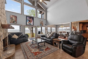 A spacious living room with large windows, a fireplace, and a dining area. - Dream Lake House 5br Sleeps 12 Tool Tx 5 Bedroom Home (Kemp)