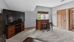 A room with a flat-screen TV, wooden cabinet, bar stools, and a window with a view. - Dream Lake House 5br Sleeps 12 Tool Tx 5 Bedroom Home (Kemp)
