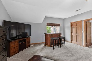 A room with a flat-screen TV, wooden cabinet, bar stools, and a window with a view. - Dream Lake House 5br Sleeps 12 Tool Tx 5 Bedroom Home (Kemp)