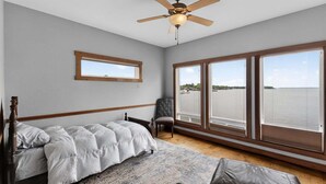 A bedroom with a bed, a chair, a ceiling fan, large windows, and a view of the water. - Dream Lake House 5br Sleeps 12 Tool Tx 5 Bedroom Home (Kemp)
