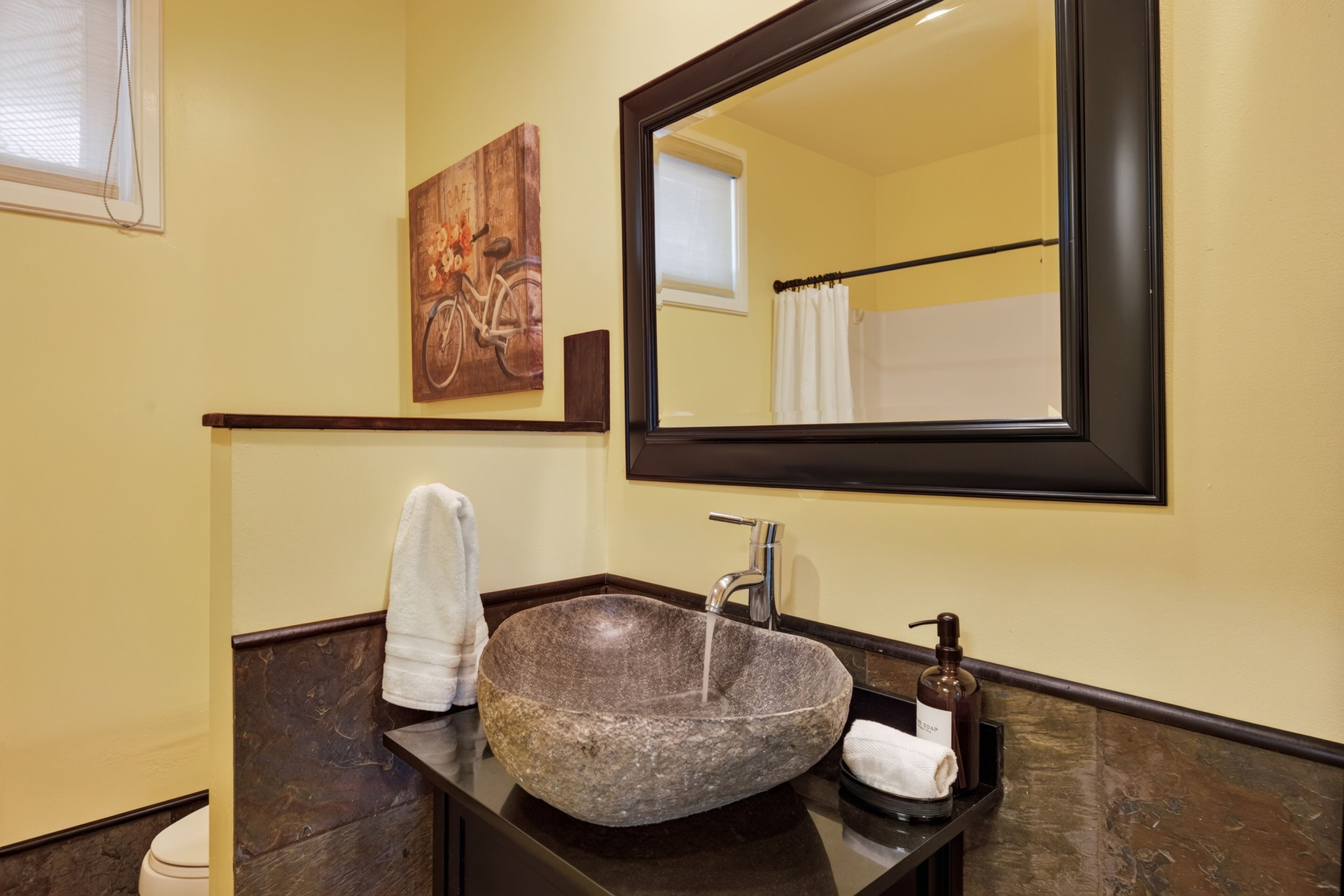 Une salle de bain avec un lavabo en pierre, un miroir, une serviette et un tableau accroché au mur.