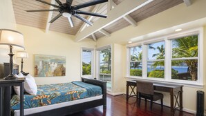Una camera da letto con un letto, una scrivania, una sedia e ampie finestre che si affacciano su palme e sull'oceano.