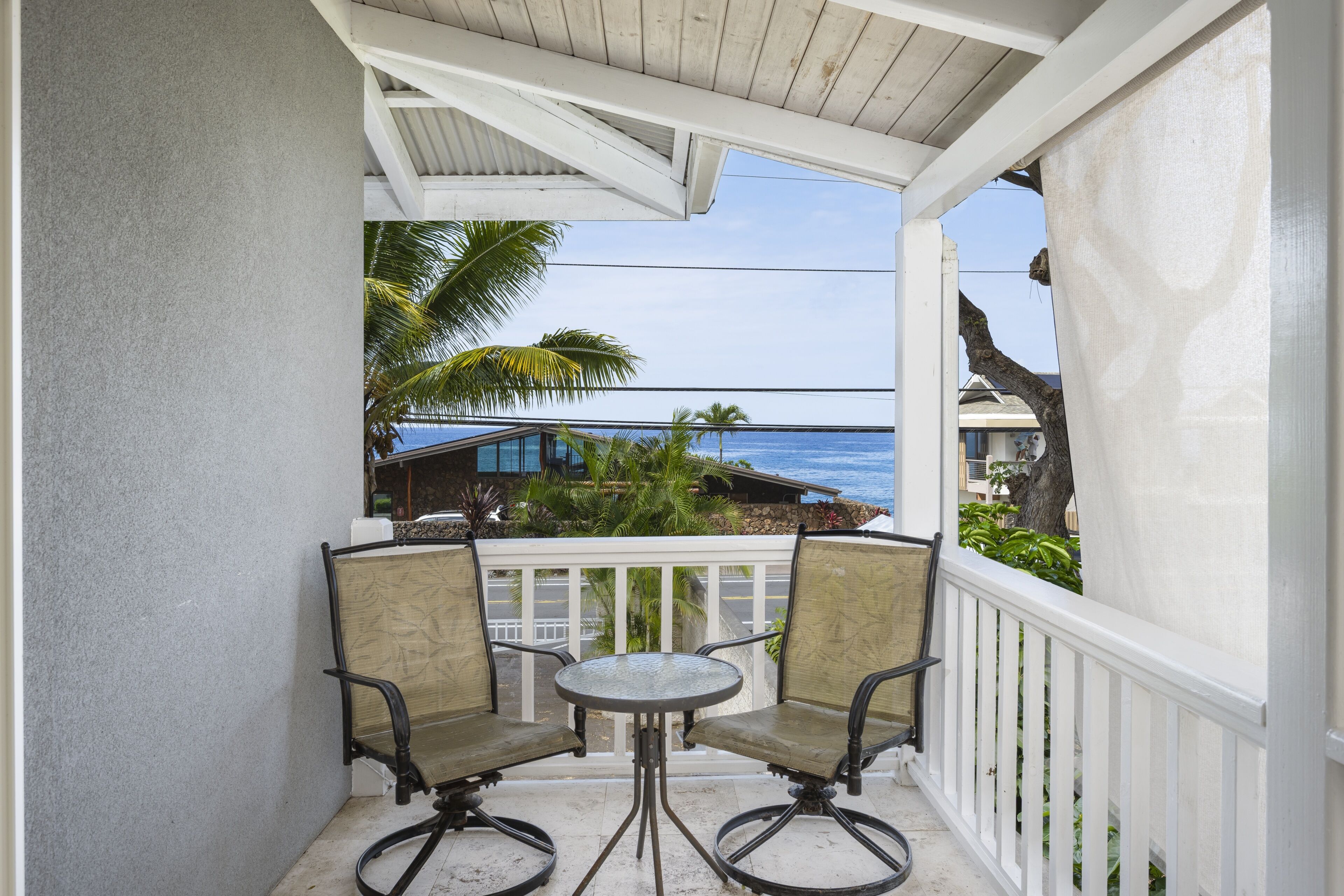 A balcony with two chairs and a table, overlooking a beach and a building.