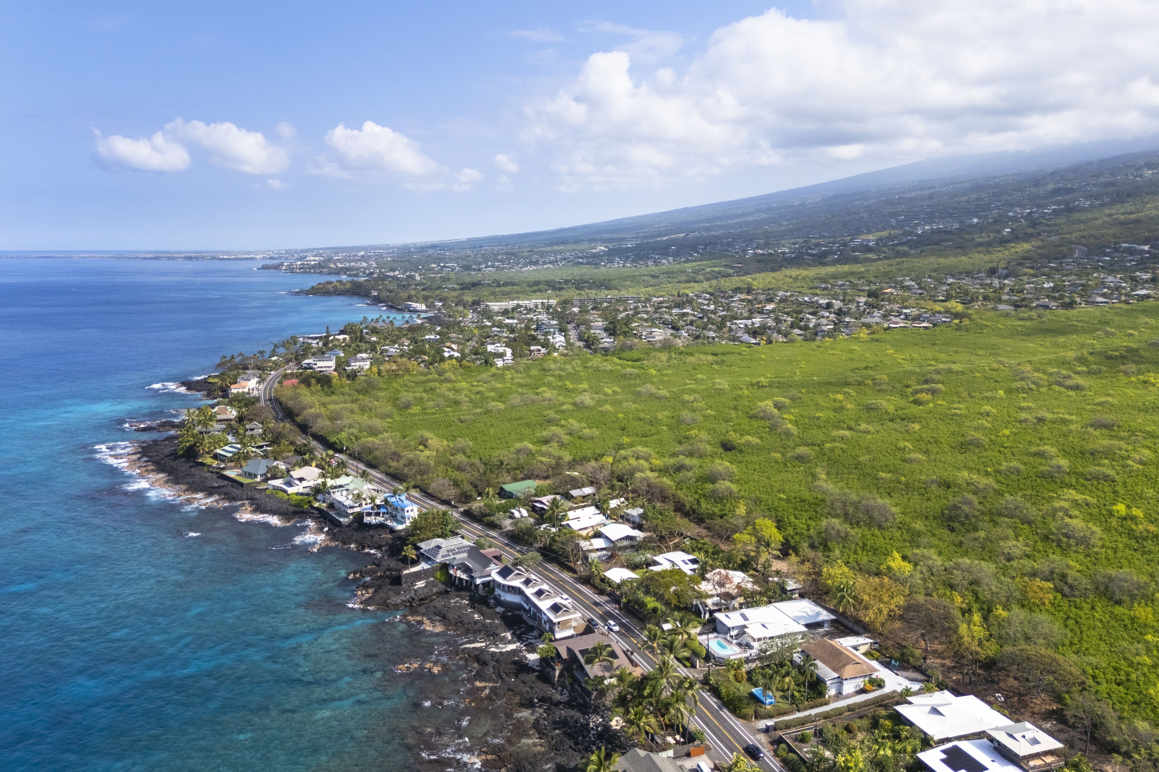 An aerial view of a coastal town with houses along the shoreline, a clear sky, and a view of the ocean.