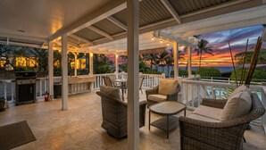 Una veranda esterna con mobili in vimini, un barbecue e vista sul tramonto.