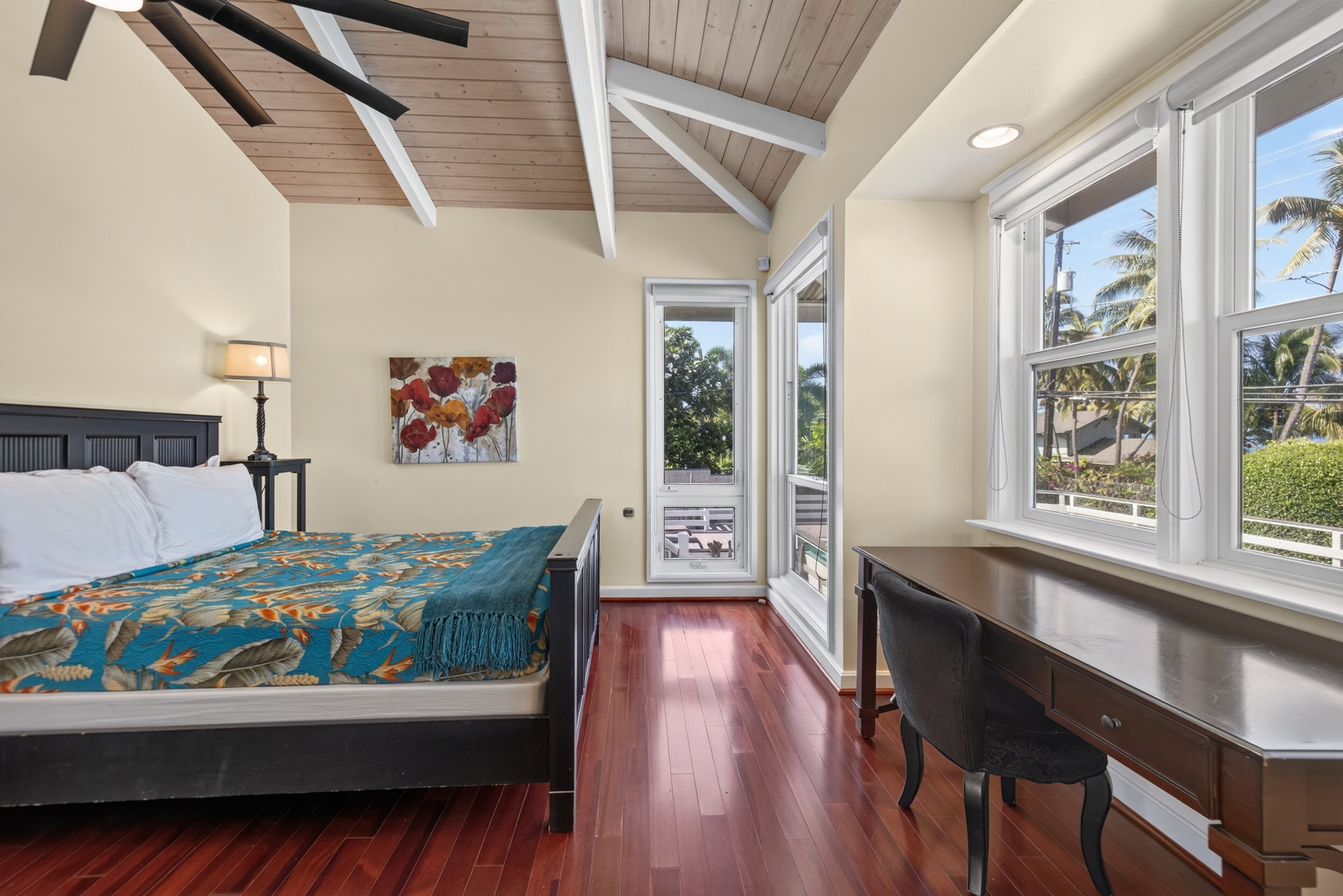 Un dormitorio con cama, escritorio, un cuadro y vistas al exterior.