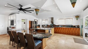 Una cucina moderna con isola centrale, zona pranzo con sedie in vimini e ventilatore a soffitto.