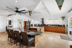 A modern kitchen with a central island, dining area with wicker chairs, and a ceiling fan. - Hale Honu 2 Bedroom Home (Kailua-Kona)