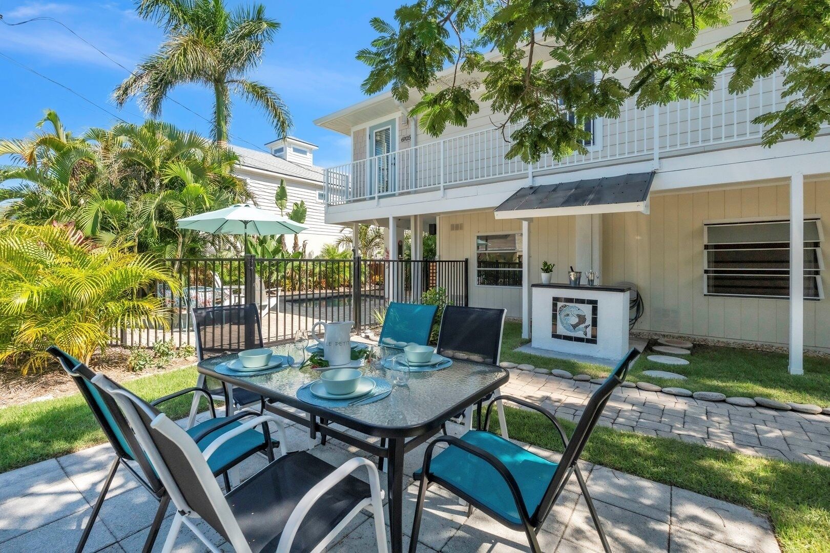 An outdoor dining area with a table set for four, surrounded by chairs, and a small patio with a grill and outdoor seating.