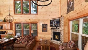 A log cabin interior with a fireplace, wooden walls, a sofa set, and a dining area. - Sherwood Love To See You Again 3 Bedroom Cabin (Pigeon Forge)