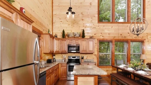A kitchen with wooden cabinetry, stainless steel appliances, granite countertops, and a dining area with a bench. - Sherwood Love To See You Again 3 Bedroom Cabin (Pigeon Forge)