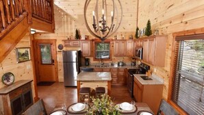 A wooden cabin interior with a dining area, kitchen, and a staircase. - Sherwood Love To See You Again 3 Bedroom Cabin (Pigeon Forge)