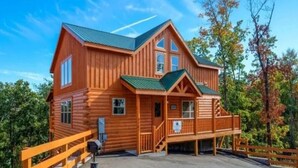 A large wooden cabin with a porch, multiple windows, and a covered staircase. - Sherwood Love To See You Again 3 Bedroom Cabin (Pigeon Forge)