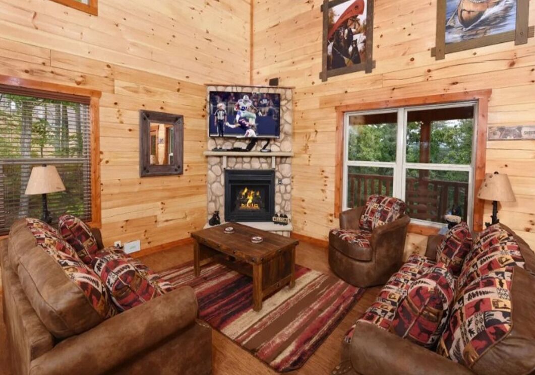 En stuga med träpanel på insidan, en steneldstad, lädersoffor, en tv och inramade tavlor på väggarna.