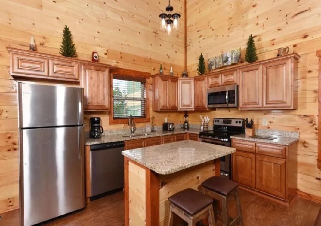 Eine Küche mit Holzschränken, einem Edelstahlkühlschrank, Granit-Arbeitsplatten und einer zentralen Kochinsel mit Sitzgelegenheiten.