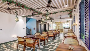 Een restaurant met houten tafels en stoelen, een vloer met een patroon, plafondventilatoren en decoratieve planten.