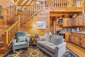 A wooden cabin interior with a staircase, a sofa, a chair, a kitchen area, and a dining table. - Bear Cub 2 - Cute Cabin in Helen, GA (Helen)