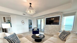 A living room with a large sofa set, a coffee table, and a chandelier. There is a view of the ocean through large windows. - 2002p 2 Bedroom Condo (Myrtle Beach)