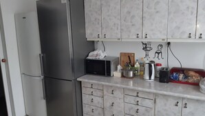 Una cocina con un refrigerador de acero inoxidable, armarios de mármol blanco, un microondas y diversos utensilios de cocina sobre la encimera.