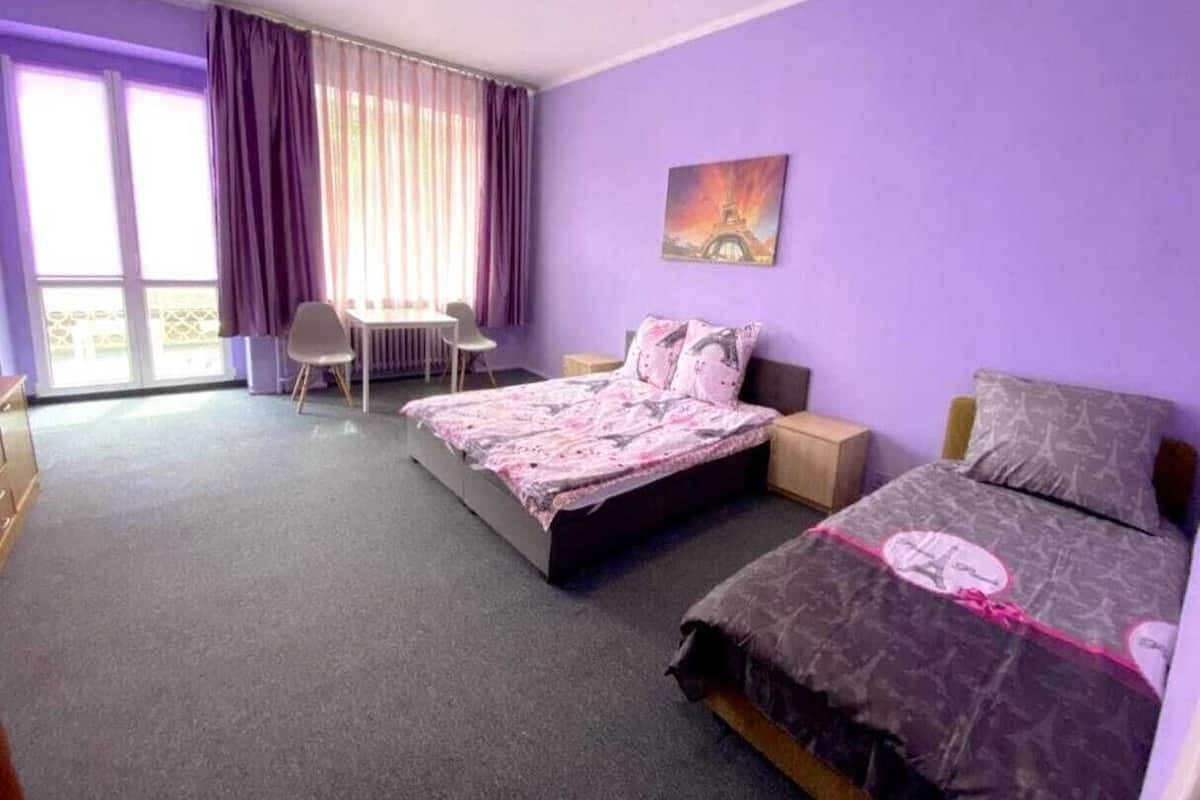 Une pièce comprenant un lit, un bureau, une chaise et une fenêtre avec des rideaux.