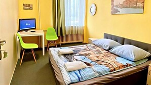 Habitación de hotel con cama, escritorio con computadora, silla, ventana con cortinas y un reloj de pared.