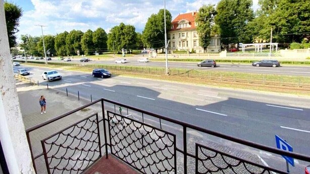 Vista de la calle con un edificio al fondo, un paso de peatones y coches en la carretera.