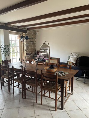 A dining area with a wooden table and chairs, a stone wall, and a window.