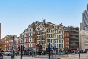 A street with historic buildings, a clear sky, and pedestrians. - Cosy Bishopsgate Suite. (London)