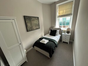 Un dormitorio con cama, una mesita de noche con lámpara, una ventana con vistas y una puerta.