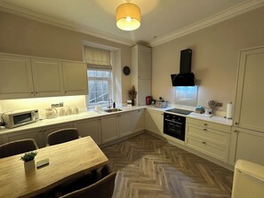 Una cocina moderna con armarios blancos, microondas, pileta y comedor con mesa y sillas.