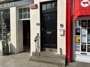 Ein Schaufenster mit einer schwarzen Tür, einem Schild mit der Aufschrift 'Artisan Bottled Beer Shop' und einer roten Markise mit einem Kuh-Logo.