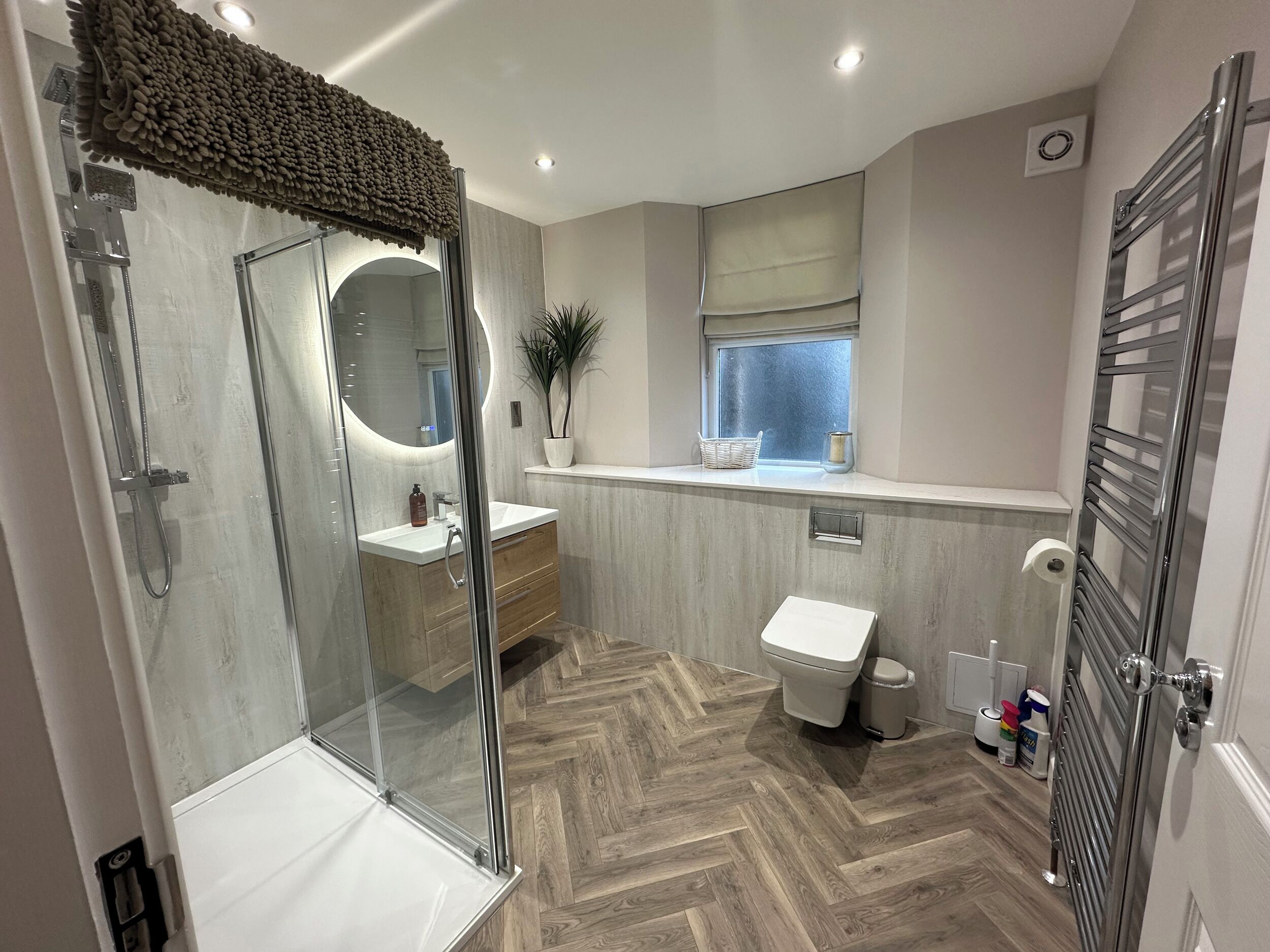 A modern bathroom with a glass shower enclosure, a vanity with a mirror, a toilet, and a window with a view.