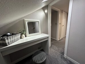 Un baño con tocador blanco, un espejo, una cesta de mimbre, una planta en maceta y un taburete a rayas.