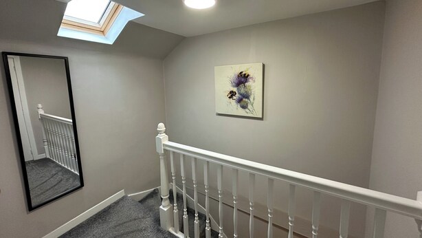 Eine Treppe mit weißer Handläufung, einem Oberlicht und einem Gemälde an der Wand.