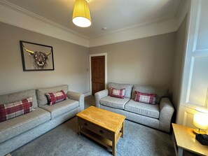 A living room with two grey sofas, a wooden coffee table, a lamp, and a bull-themed artwork on the wall. - The Teviot (Melrose)