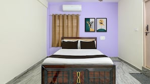 Un dormitorio con una cama, un ventilador de techo, una ventana con cortinas y dos cuadros en la pared.