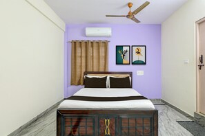 Ein Schlafzimmer mit einem Bett, einem Deckenventilator, einem Fenster mit Vorhängen und zwei gerahmten Bildern an der Wand.