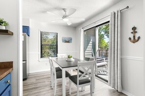 Comedor con mesa, sillas, ventilador de techo y vista a una terraza exterior por medio de un ventanal corredero.