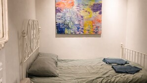 Habitació petita i acollidora amb un llit, un sofà, una taula petita i un quadre abstracte i colorit a la paret.